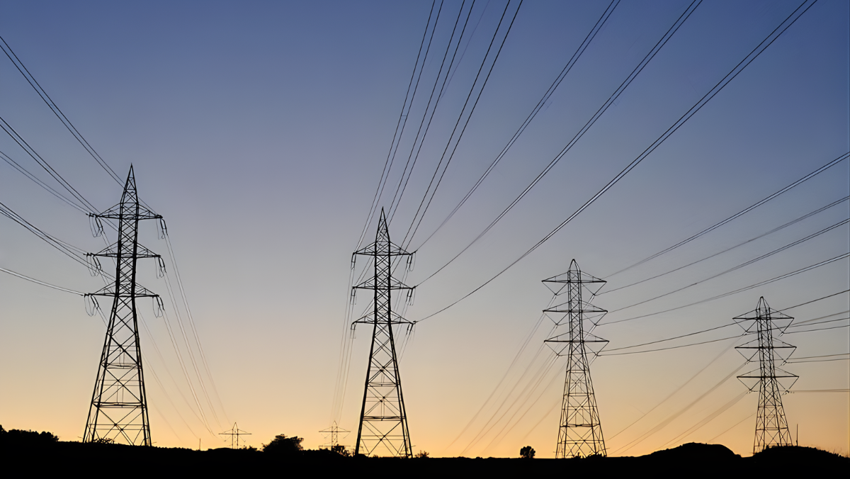 High-voltage transmission towers and power lines at sunset across an open landscape