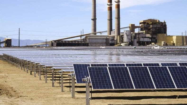 Utility scale solar array with power plant in background
