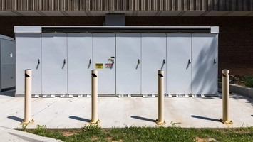 Grey electrical utility enclosure with warning signs and bollards