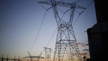 Electricity transmission towers and power lines silhouetted against a blue and orange twilight sky at dusk