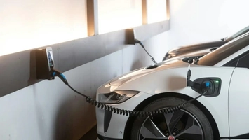 White electric cars connected to wall-mounted charging units via coiled cables in an indoor parking space